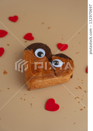 Funny creative eyes on Heart shaped dark chocolate croissant on beige background with copy space. Puff pastry new trendy sweet dessert bakery. Creamy dough Funny creative eyes on Heart shaped dark chocolate croissant on beige background with copy space. Puff pastry new trendy sweet dessert bakery. Creamy dough 132970697