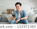 Smiling handsome young Asian man sitting on cozy couch 132971365