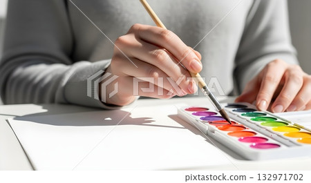 Closeup of hands painting with watercolors on a white surface. 132971702
