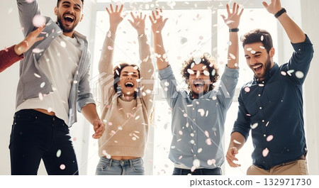 Joyful friends celebrating with confetti indoors, raising arms high 132971730