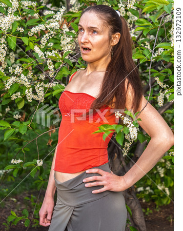 Young woman sneezes in the park against the background of a flowering tree. Allergy to pollen concept. Young woman sneezes in the park against the background of a flowering tree. Allergy to pollen concept. 132972109