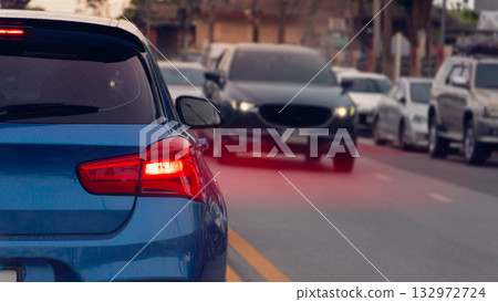 Luxury of blue car on the road with speed light red color from brake. Other car driving passthrough from opposite lens. and many cars parking side of asphalt road. 132972724