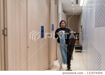 woman holding clothes in fitting room hallway 132974409