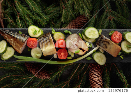 Smoked mackerel with fresh cucumbers, tomatoes and green onions on a black plate. 132976176