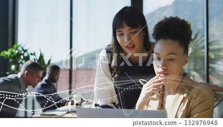 Collaborating business professionals leaning over laptop in office meeting room, with coffee mugs 132976948