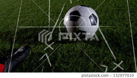 Resting soccer ball sitting on grass pitch under lights, with red sock cleat, white chalk tactics Resting soccer ball sitting on grass pitch under lights, with red sock cleat, white chalk tactics 132977010