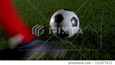 Swinging leg wearing red sock sending soccer ball rolling on floodlit turf with graph overlay 132977011