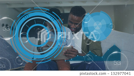Smiling father and son exploring superimposed 5G data overlays on home sofa, with tablet computer Smiling father and son exploring superimposed 5G data overlays on home sofa, with tablet computer 132977041