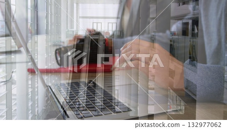 Typing adult on laptop at wooden desk in atrium, with escalator, red floor runner, glass windows 132977062