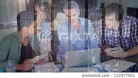 Three men using laptop tablet checking smartphone amid printed charts, glass reflection in office 132977063