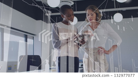 Colleagues wearing office attire analyzing data on handheld device in office, with chart overlay 132977077