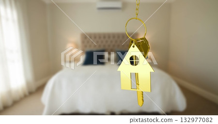 Dangling golden house-shaped keychain holding two metal keys in bedroom, with tufted headboard Dangling golden house-shaped keychain holding two metal keys in bedroom, with tufted headboard 132977082