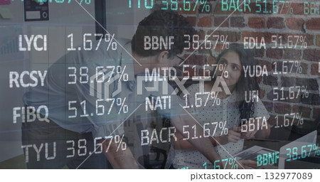 Office colleagues reviewing stocks on laptop at office desk with financial graphics Office colleagues reviewing stocks on laptop at office desk with financial graphics 132977089