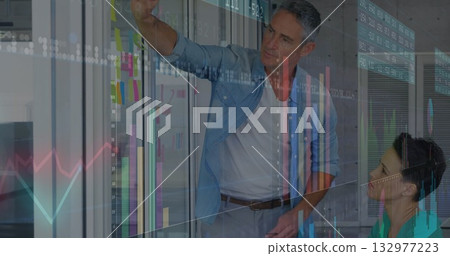 Collaborating colleagues marking sticky notes on glass partition in office, with marker and charts Collaborating colleagues marking sticky notes on glass partition in office, with marker and charts 132977223