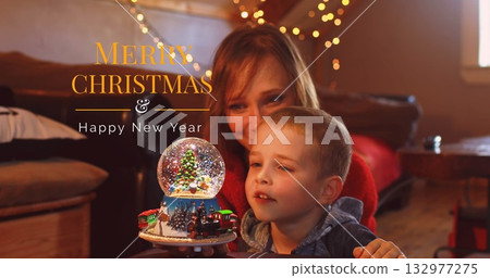 Mother and son wearing red sweater, hoodie holding snow globe in living room, with fairy lights Mother and son wearing red sweater, hoodie holding snow globe in living room, with fairy lights 132977275