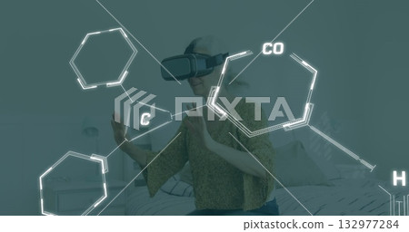 Exploring senior woman wearing virtual reality headset interacting with hexagon overlays in bedroom Exploring senior woman wearing virtual reality headset interacting with hexagon overlays in bedroom 132977284