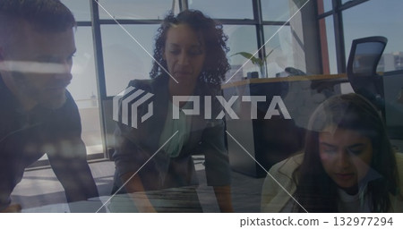 Leaning woman in gray blazer examining laptop on wooden table in office, with city skyline windows 132977294