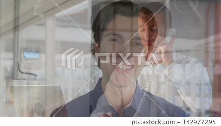 Smiling man wearing button-up shirt facing viewer in server room, with racks and telephone handset 132977295
