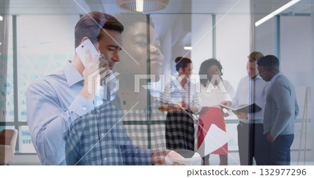 Taking call mid adult man holding smartphone, reviewing reports in glass office with pendant lamp Taking call mid adult man holding smartphone, reviewing reports in glass office with pendant lamp 132977296