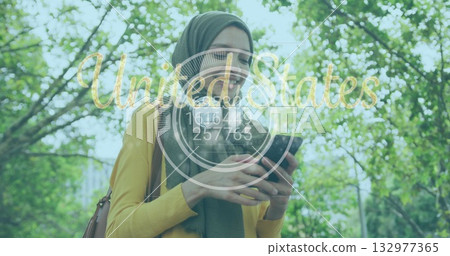 woman wearing green headscarf, yellow top holding smartphone and bag in park, United States overlay 132977365