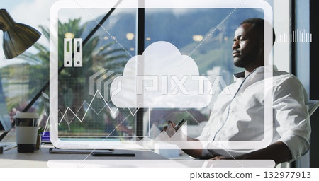 Gazing man in white shirt holding stylus in office at desk near window, with digital icons 132977913