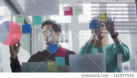 Data analysts collaborating in office with glass partition, using sticky notes and red pie piece Data analysts collaborating in office with glass partition, using sticky notes and red pie piece 132977918