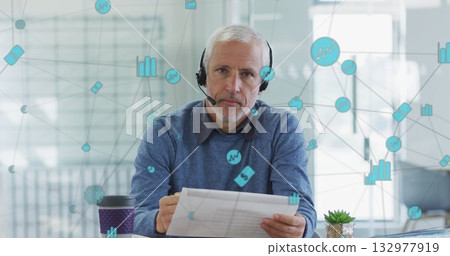 Reading consultant wearing headset and holding papers at office desk, with network icons 132977919