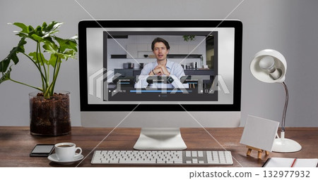 Streaming man in button-up shirt gesturing on desktop monitor at home with coffee cup, keyboard Streaming man in button-up shirt gesturing on desktop monitor at home with coffee cup, keyboard 132977932