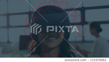 Smiling woman wearing virtual reality headset exploring virtual environment in open office space 132978062