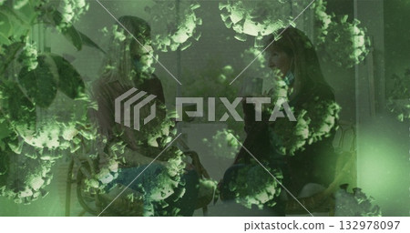 Chatting mother and adult daughter holding mugs in living room by window, with green virus overlay 132978097