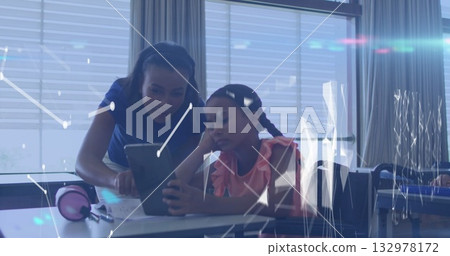Collaborating teacher and student focusing on tablet screen at school desk, with pink headphones 132978172