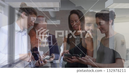 Seven professionals standing near window in modern workspace, sharing smartphone and tablet screens Seven professionals standing near window in modern workspace, sharing smartphone and tablet screens 132978211