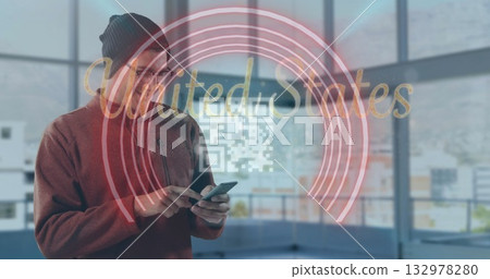 Man wearing beanie viewing AR rings and UnitedStates QR code with smartphone in office, copy space 132978280