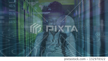 Monitoring woman IT technician in shirt checking tablet in server rack aisle, with HUD overlays Monitoring woman IT technician in shirt checking tablet in server rack aisle, with HUD overlays 132978322