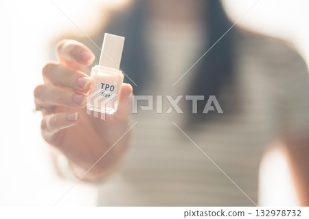 Woman holding a bottle of TPO free gel polish in bright natural light. Safe manicure product without Trimethylbenzoyl Diphenylphosphine Oxide for health-conscious consumers. Woman holding a bottle of TPO free gel polish in bright natural light. Safe manicure product without Trimethylbenzoyl Diphenylphosphine Oxide for health-conscious consumers. 132978732