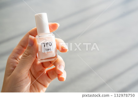Woman holding a bottle of TPO free gel polish in bright natural light. Safe manicure product without Trimethylbenzoyl Diphenylphosphine Oxide for health-conscious consumers. 132978750