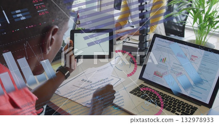 Reviewing coworker holding tablet and stylus pen at office desk with laptop and plant, copy space 132978933