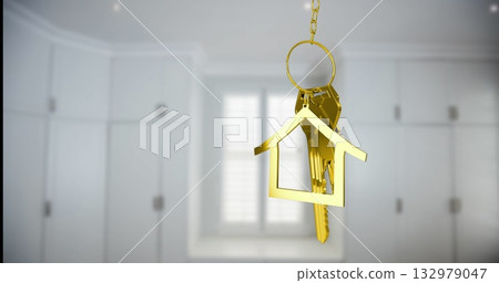 Hanging gold house-shaped keychain swinging gently in kitchen entryway, with metal keys and chain 132979047