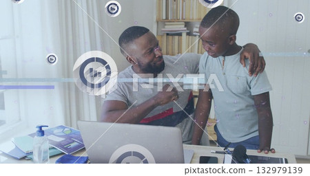 Fist bumping father and son sharing supportive gesture at home office desk, with laptop and charts 132979139