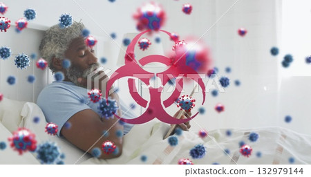 Propping chin, man in light blue t-shirt viewing tablet on bed, with virus and biohazard graphics 132979144