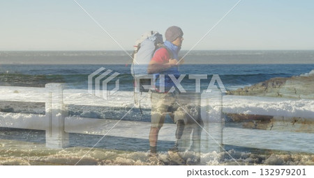 Standing hiker gazing at crashing waves behind railing coastal walkway with backpack, copy space 132979201