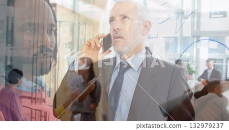 Speaking senior executive wearing suit on smartphone in corporate office, with glass board diagrams 132979237