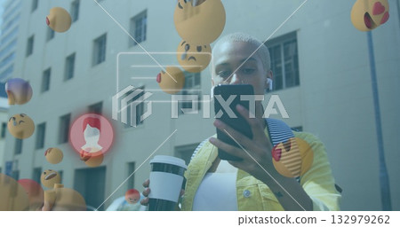 Standing woman holding smartphone and coffee cup on sidewalk, with earbuds, emojis and chat overlay 132979262
