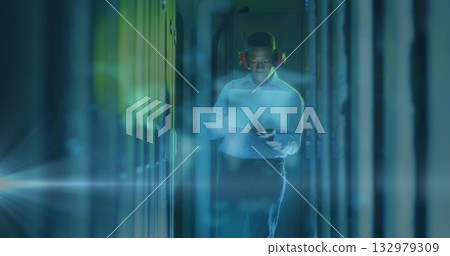 Walking IT technician checking server racks in data center aisle, with tablet, hearing protection 132979309