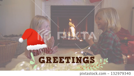 Siblings playing clapping game in living room with lit fireplace, hanging stocking on marble mantel 132979340