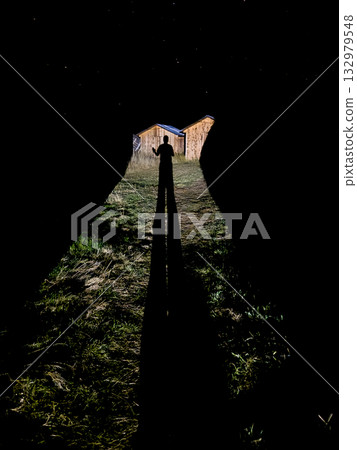 Silhouette at the end of a dark tunnel leading to lit cabins under a starry night 132979548