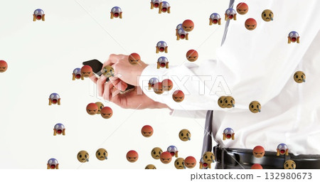 Standing man in suit holding smartphone in studio, amid angry shocked worried icons, copy space Standing man in suit holding smartphone in studio, amid angry shocked worried icons, copy space 132980673