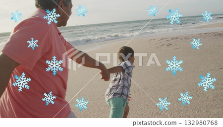 Grandfather in coral polo, grandson in plaid holding hands running on beach, with blue snowflakes 132980768