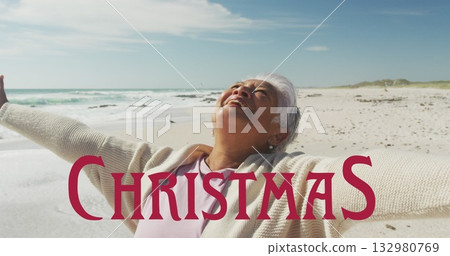 Breathing senior Asian woman in pale pink shirt and cream cardigan at beach, with Christmas graphic 132980769