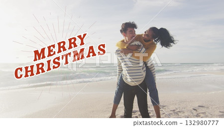 Carrying woman on back on sandy beach wearing casual clothes, with red MERRY CHRISTMAS text 132980777